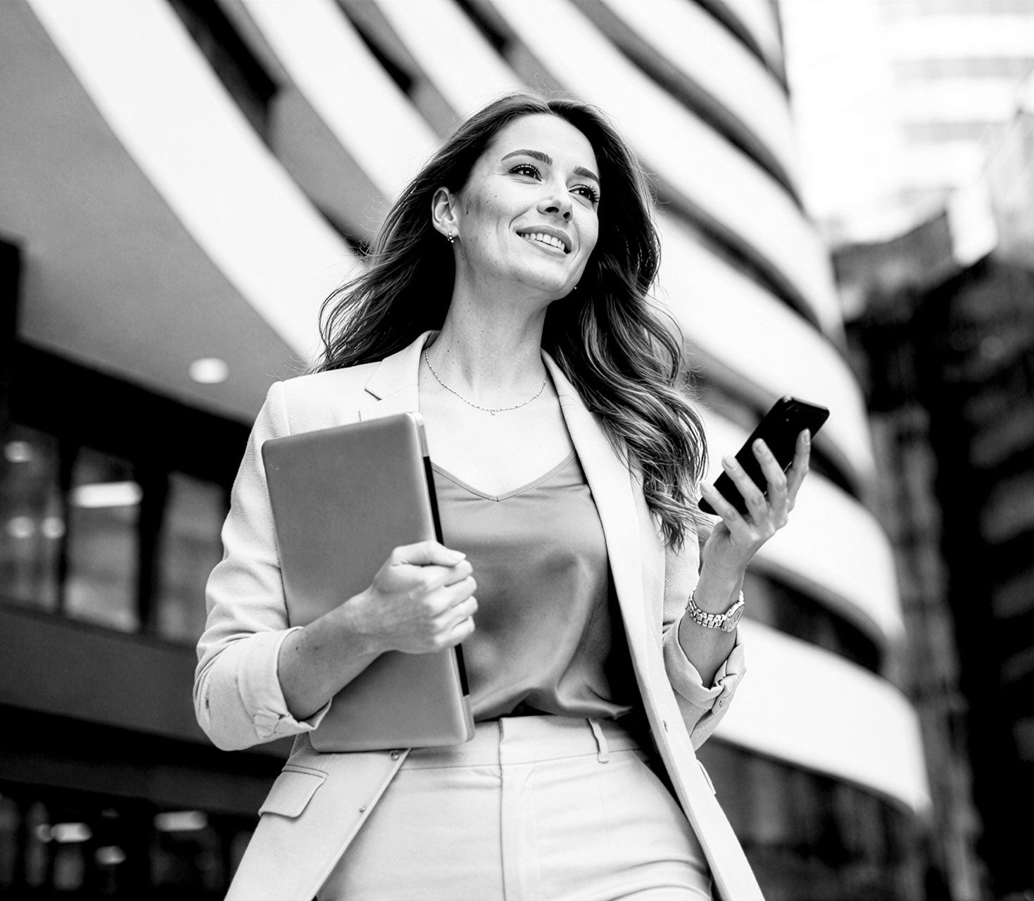 Personne tenant une tablette et un smartphone devant un bâtiment moderne, dans un environnement professionnel urbain en noir et blanc.